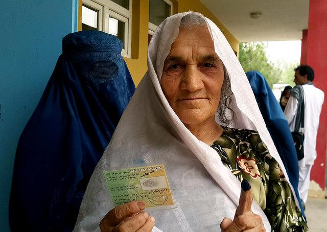 A elderly woman shows her inked finger and voting card